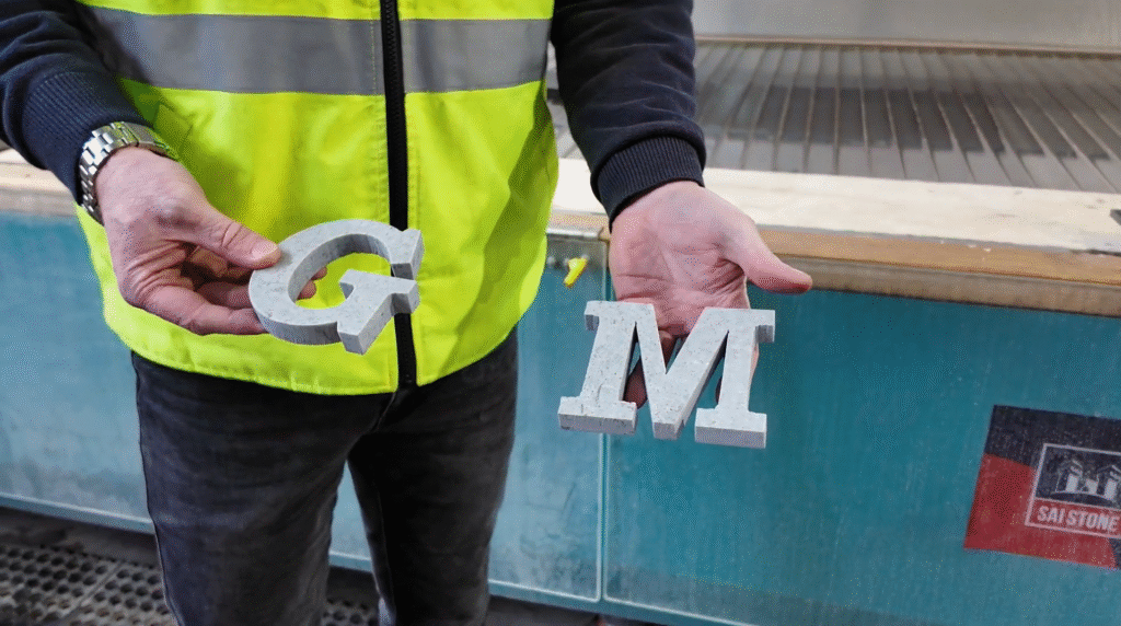 Worker holds custom-cut stone letters "G" and "M" produced using high-precision waterjet technology at SAI Stone facility
